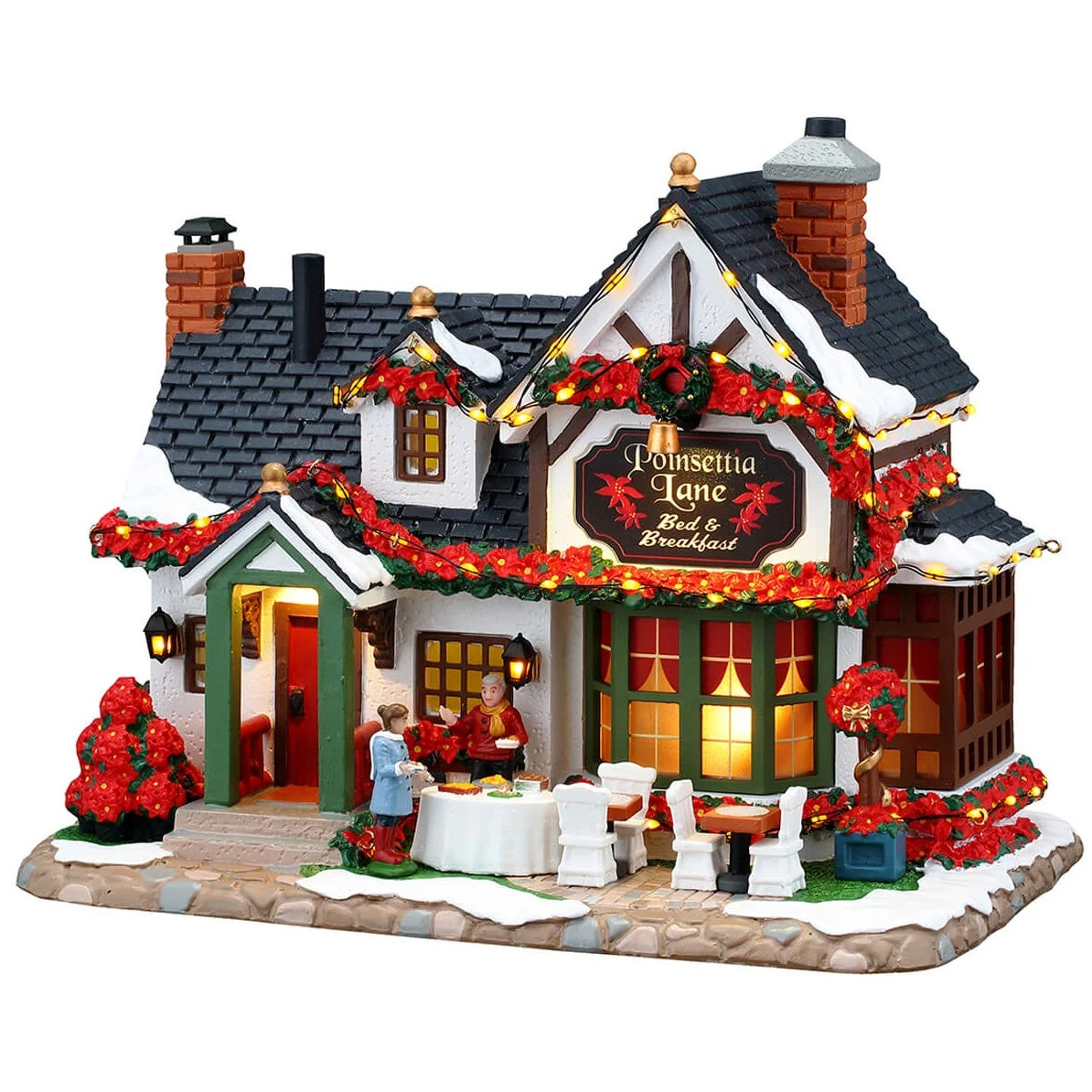 This image shows what this Lemax building looks like on a white background. It was designed to look like a bed and breakfast house. The roofline is covered in a poinsettia garland and lights. There are tables outside and people are decorating them with poinsettias.