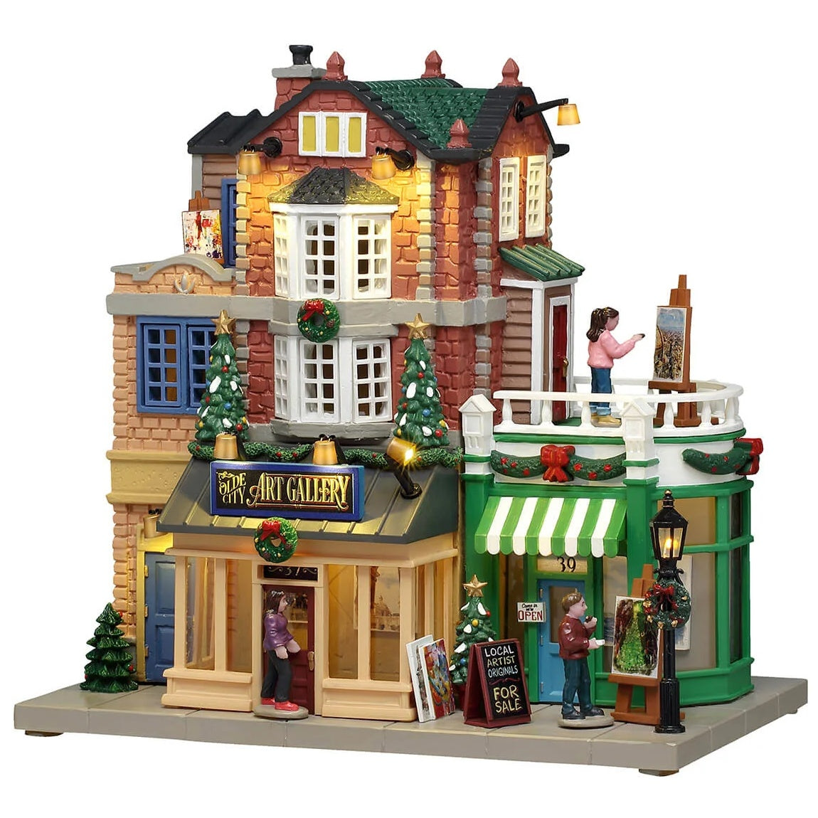 This image shows what this Lemax building looks like on a white background. It was designed to look like a tall art gallery. There's a balcony on the second floor where there's a woman painting. There are people on the sidewalk looking at the art that's on display outside. There are decorated Christmas trees and wreaths all over.