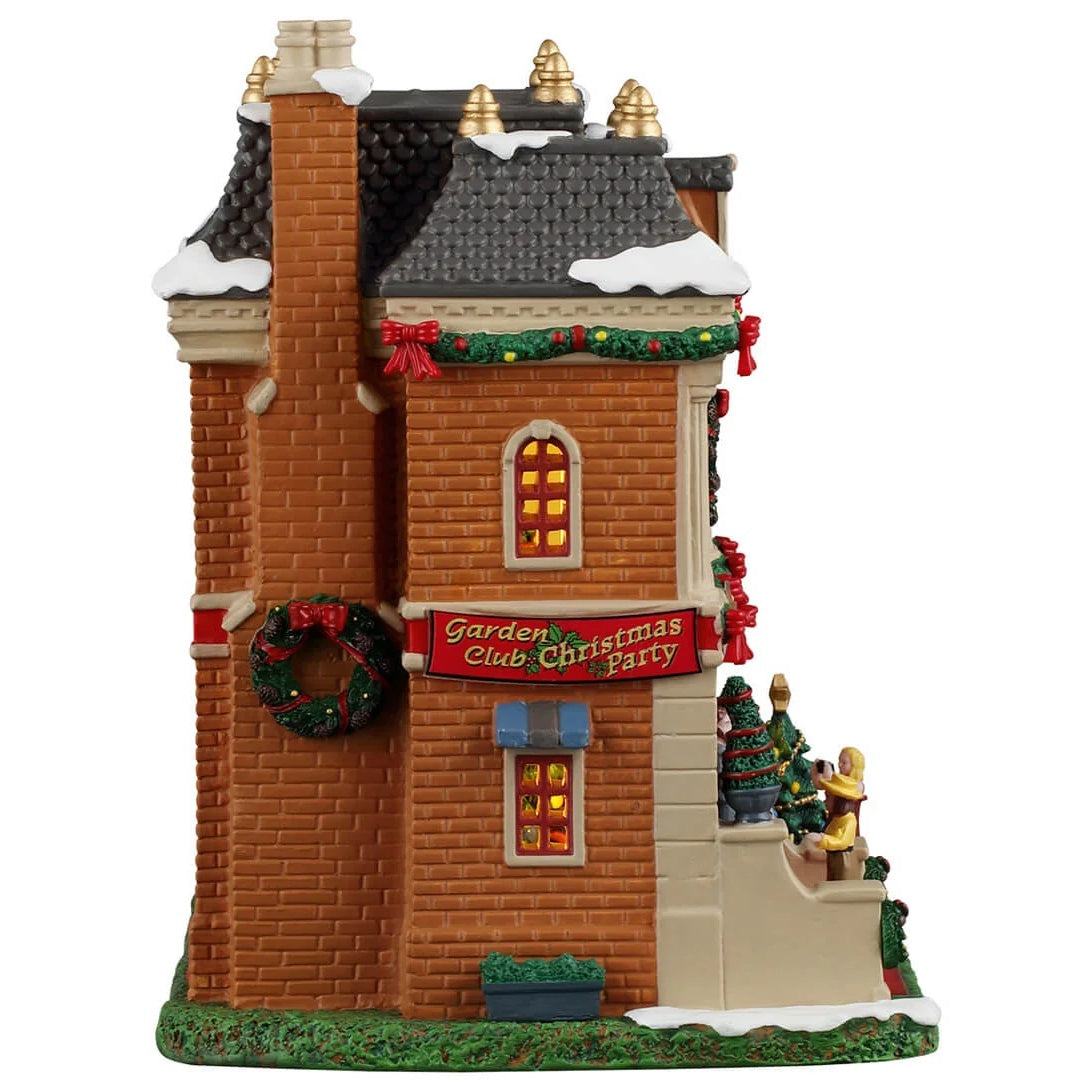 This image shows what the side of this building looks like. There's a large decorated wreath hanging on the chimney and a large red sign that reads "Garden Club Christmas Party."