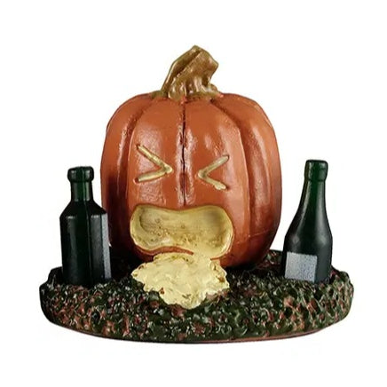 This Lemax accessory looks like a jack-o-lantern on a grassy patch. There's a green bottle on the left of the pumpkin and on the right. This pumpkin looks like it has thrown up.