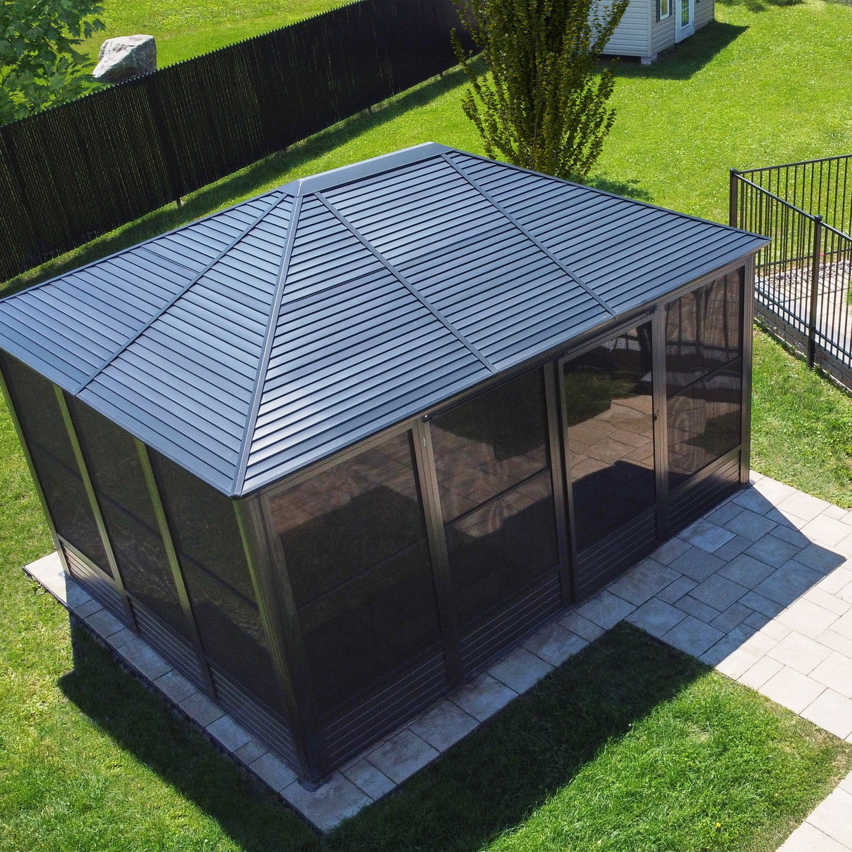 This image shows what this gazebo looks like in a backyard from above on a very sunny day. The color is a rich, deep charcoal-gray. It was built on a stone patio in a grassy backyard.