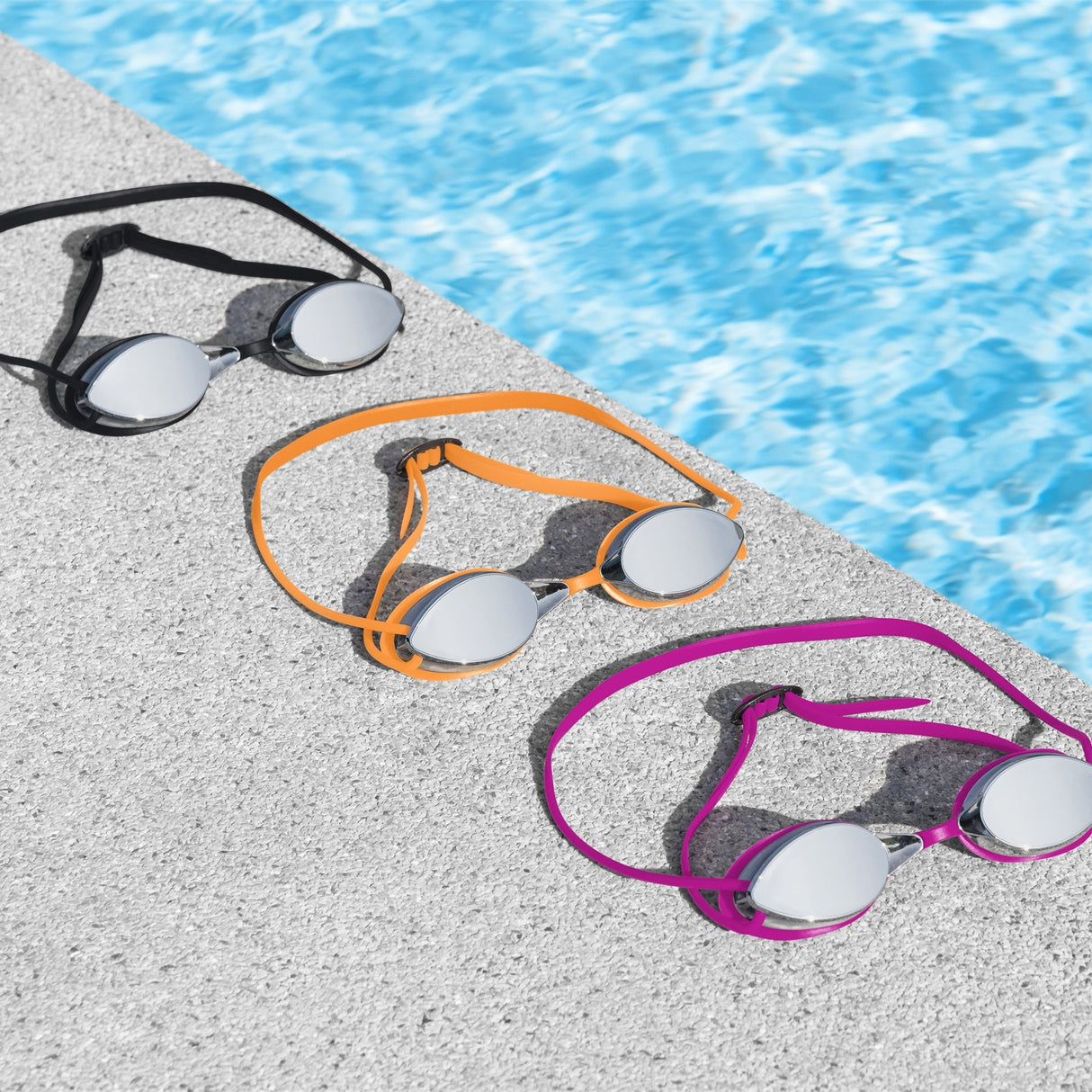 This is a lifestyle image showing all three of the color options available for these googles, laid out on the edge of a pool.