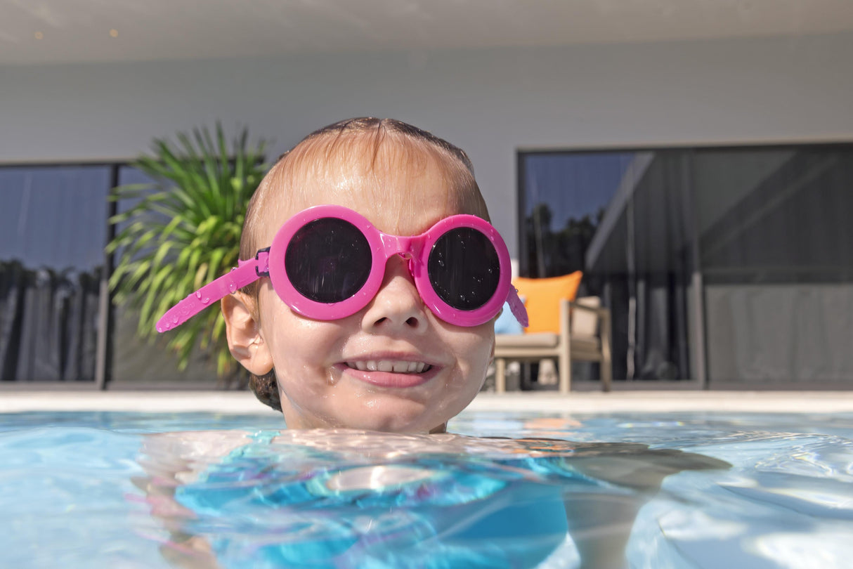This is a lifestyle image showing a young girl posing with her head above water wearing the neon pink colored goggles.