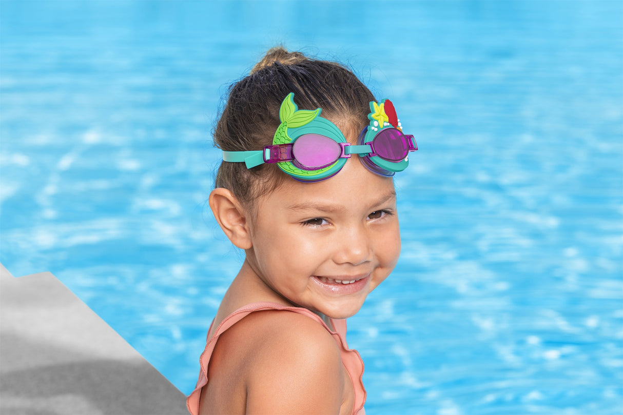 This is a lifestyle image showing a young girl wearing the mermaid themed goggles while sitting on the edge of a pool.