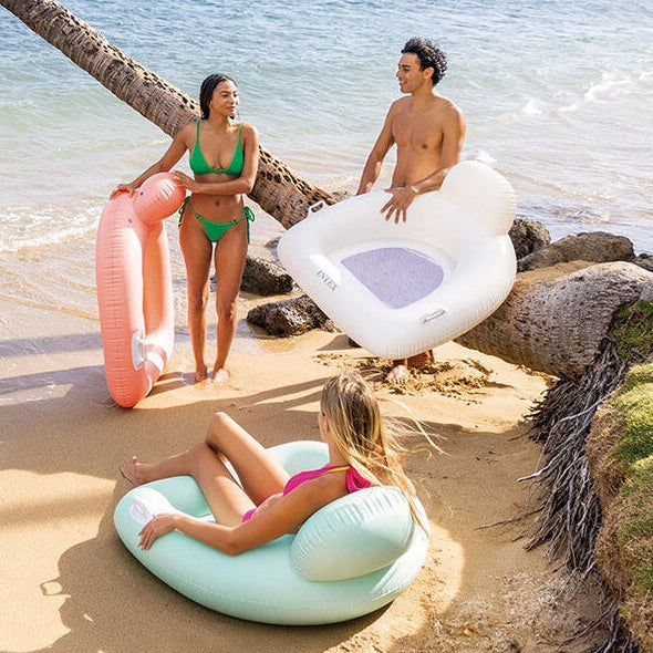 This is a lifestyle image showing three adults on a beach holding these inflatable chairs.