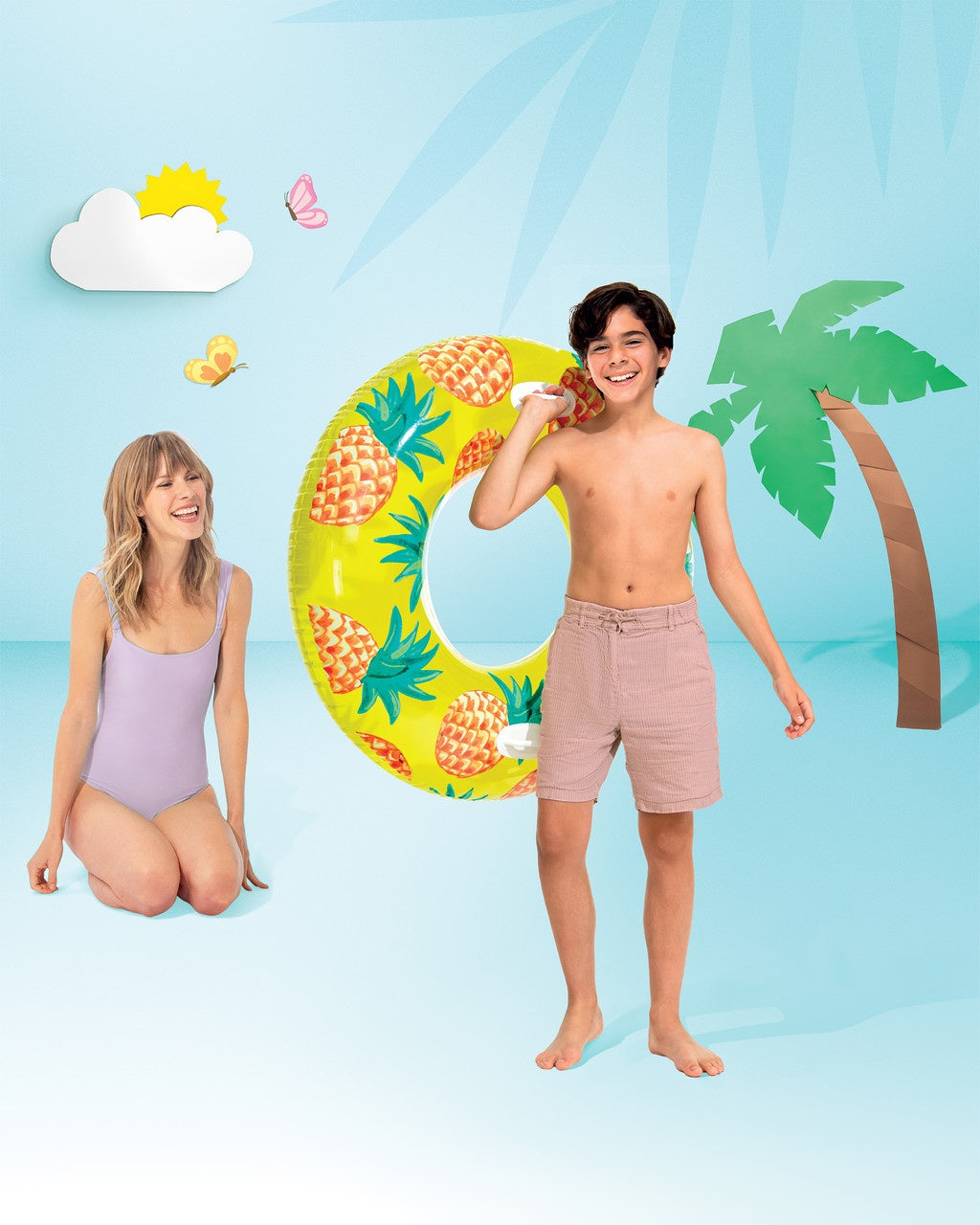 This is a lifestyle image showing a young boy holding the pineapple inner tube on a set that is designed to look like a beach made out of paper.