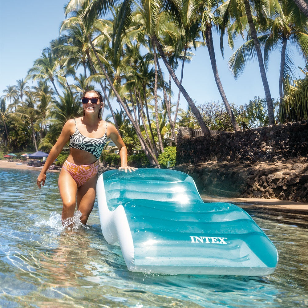 This is a lifestyle image showing a woman standing next to this inflatable chair in the ocean on a beach.