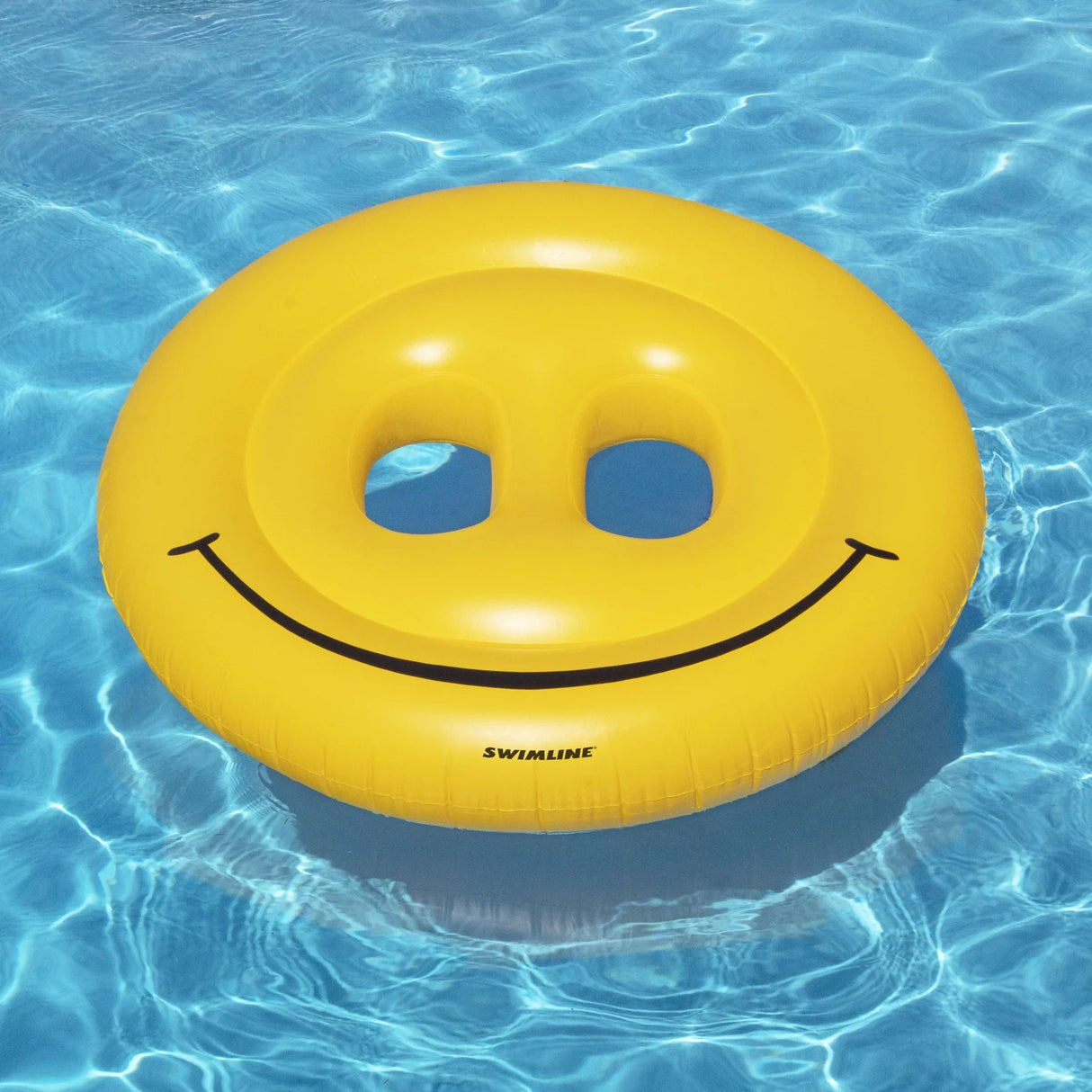 This is a lifestyle image showing the Swimline smiley face pool inflatable floating on the surface of a pool.