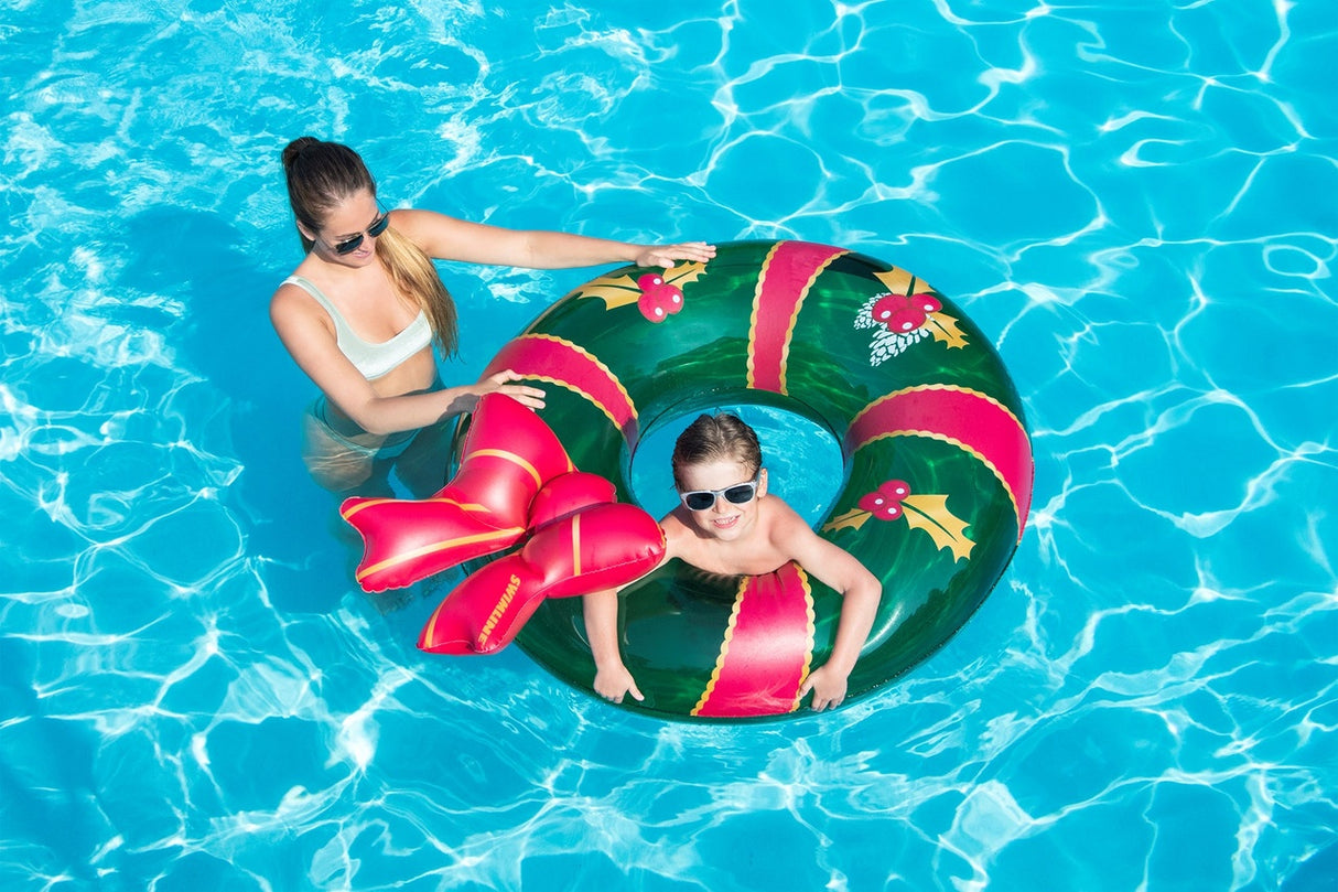 This is a lifestyle image showing a little boy inside the wreath inner tube while his mom holds the inner tube in a pool.