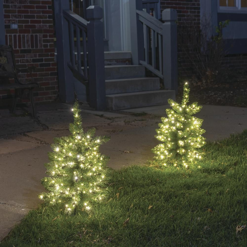 This is a lifestyle image showing the tree pre-lit artificial trees lining a pathway near a front door.