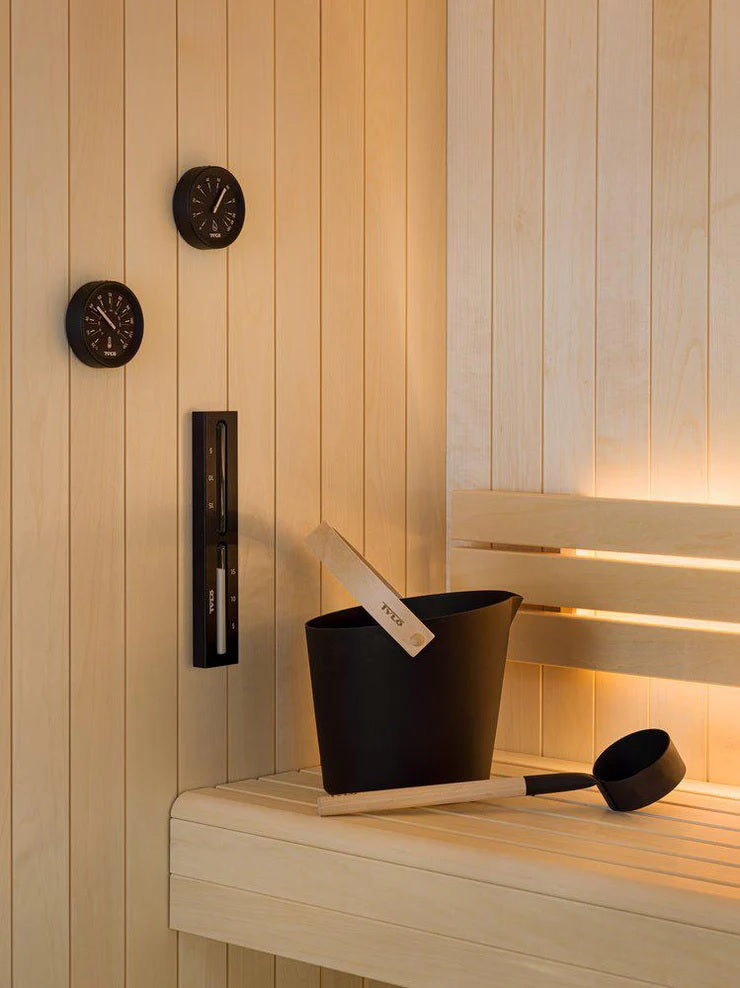This lifestyle image shows a sauna bucket and a sauna ladle inside of a sauna resting on a bench.