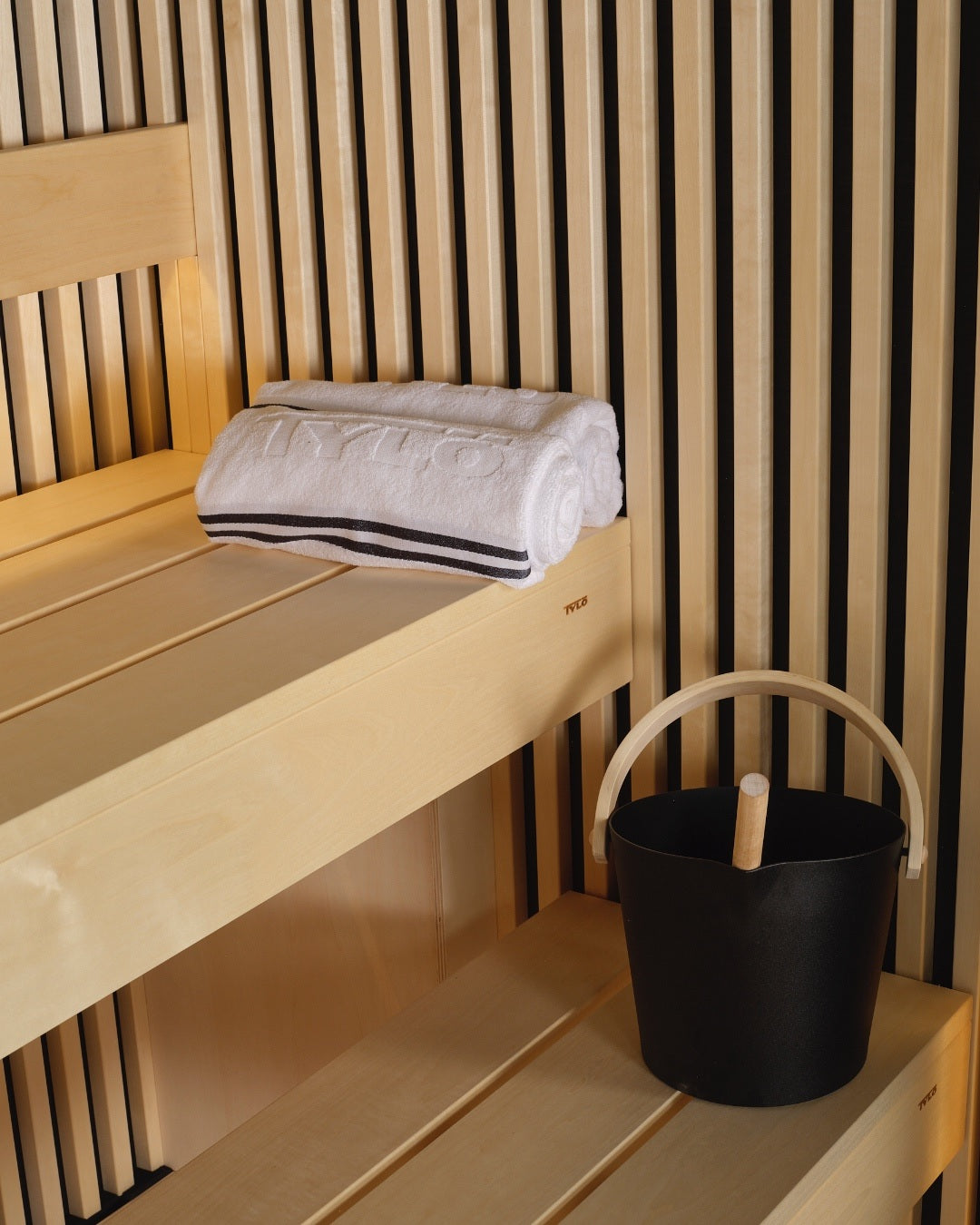 This lifestyle image shows inside a sauna with the sauna bucket resting on one of the benches.