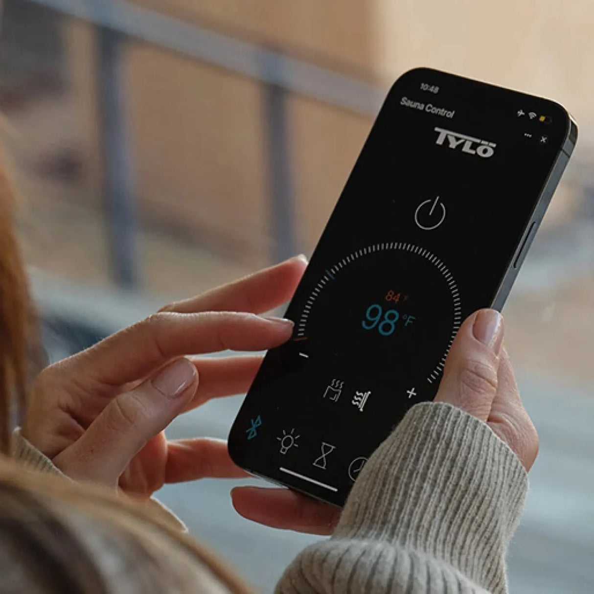 This image shows a person controlling the temperature inside the sauna with an app on a phone.