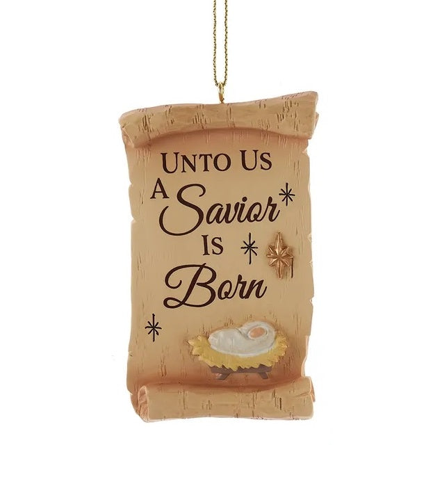 This image shows a brown scroll ornament that reads "UNTO US A SAVIOR IS BORN" and features baby Jesus in a manger.