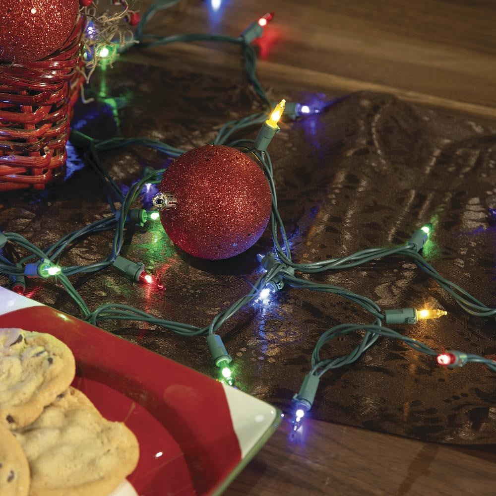 This is a lifestyle image showing the multi-colored twinkling lights on a green wire on a gray table runner.