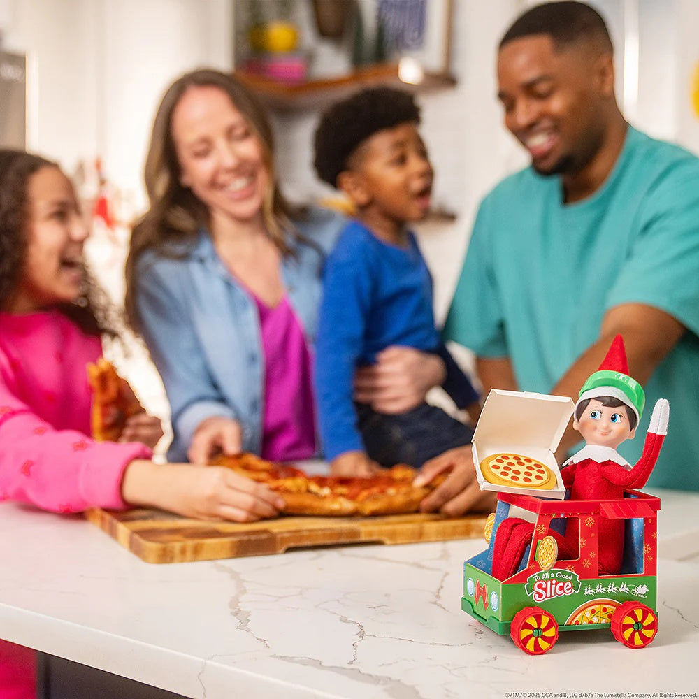 This is a lifestyle image showing a family enjoying a pizza in the kitchen while a Scout Elf in the pizza truck watches.