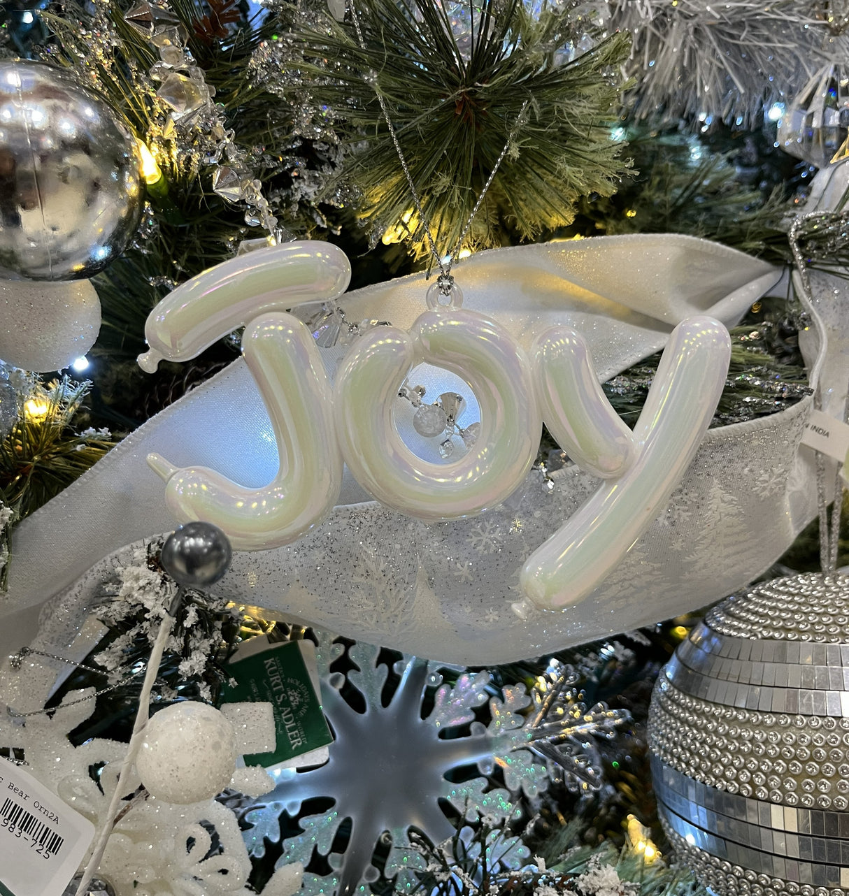 This is a lifestyle image showing the Joy Balloon Ornament on a tree decorated with other white and silver decorations.
