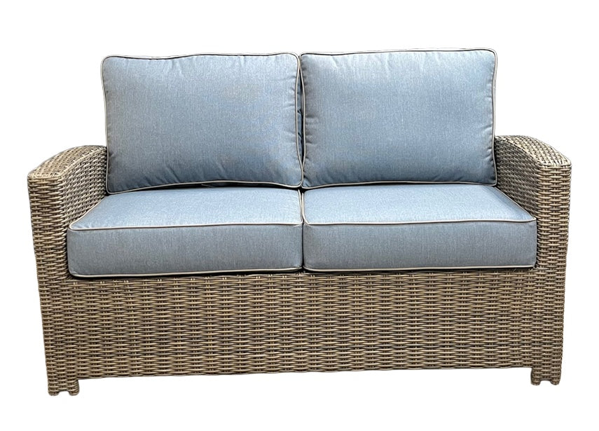 This image shows what this loveseat looks like on a white background. The frame is a tan/brown wicker color. The cushions are a light blue color.