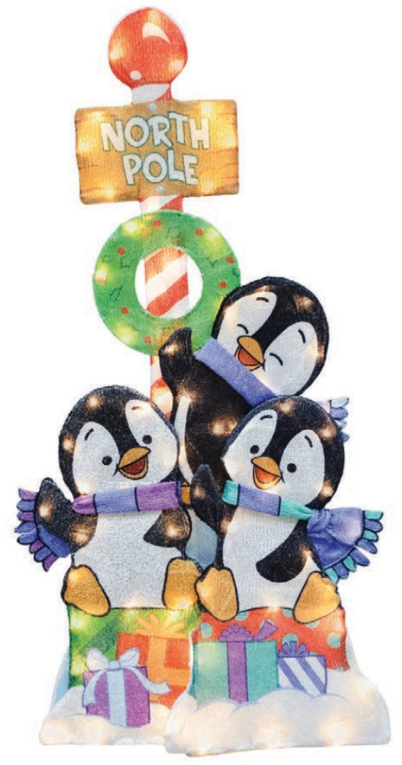 This image shows this decoration on a white background. There are three playful penguins sitting on a bunch of presents. There's a North Pole sign with a wreath behind them.