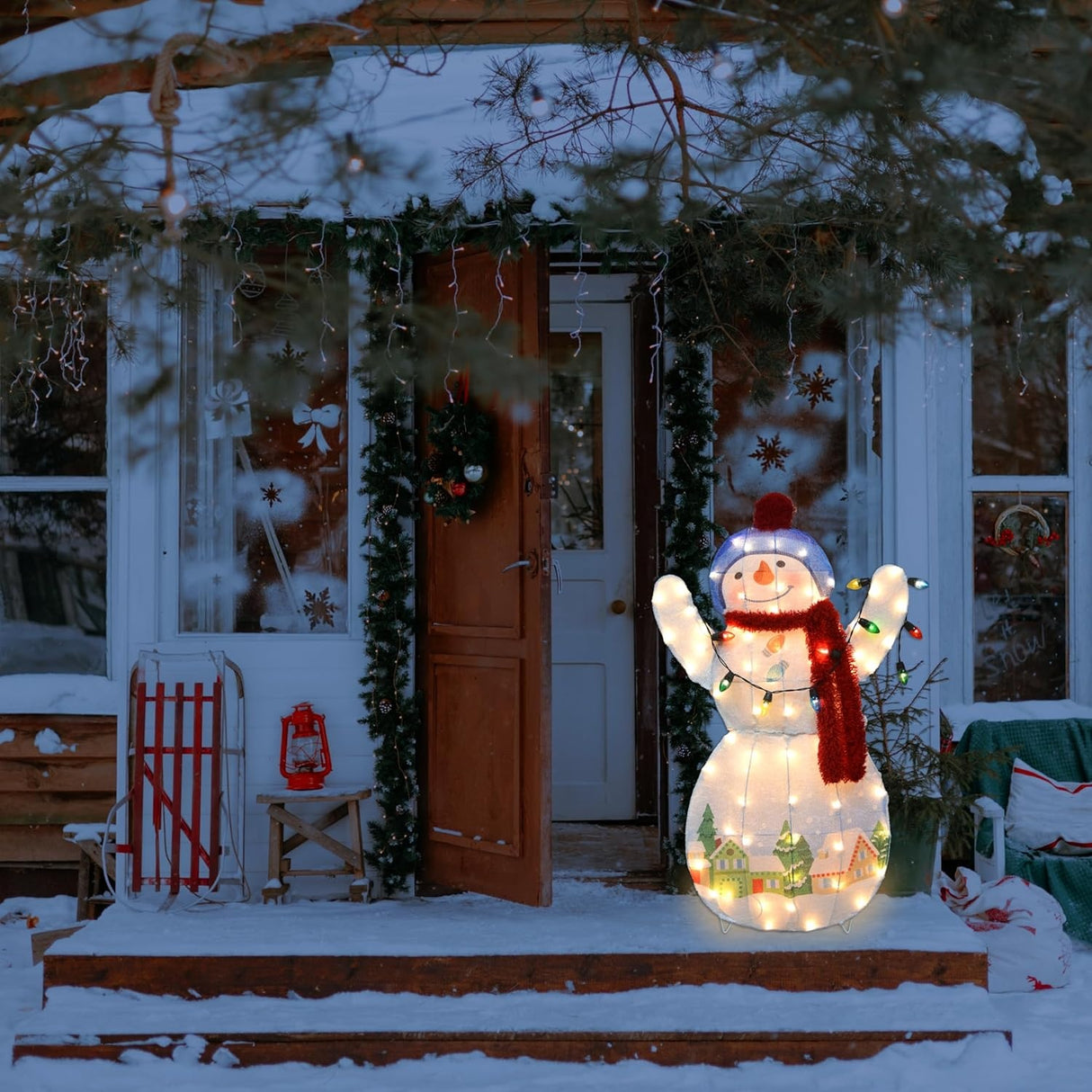 This is a lifestyle image showing the snowman sculpture on a snowy front porch next to a front door.