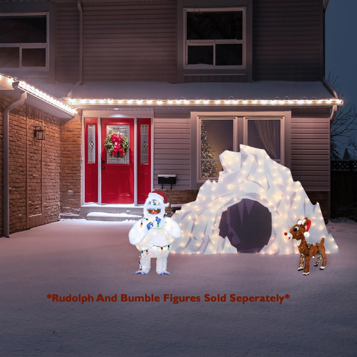 This is a lifestyle image showing the cave on a snowy lawn in front of a house decorated for Christmas. Next to the cave on the left is a Bumble decoration. Next to the cave on the right is a Rudolph decoration. Rudolph and Bumble figures are sold separately.