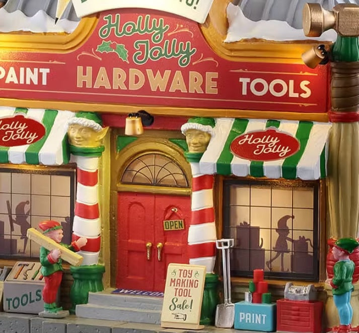 This is an up close view of the building. The awnings are green and white striped and the columns next to the door are red and white striped and there are elf faces up top. You can see two elves working on the sidewalk outside.