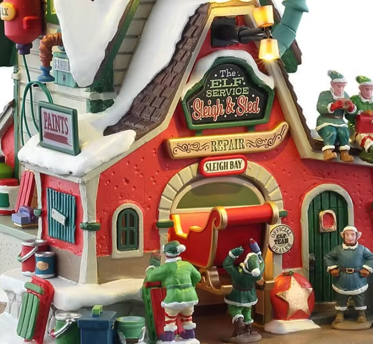 This is an up close view of this building. There are signs that read "PAINTS" and "THE ELF SERVICE SLEIGH & SLED" and "REPAIR" and "SLEIGH BAY." There are sleds and cans of paint everywhere.