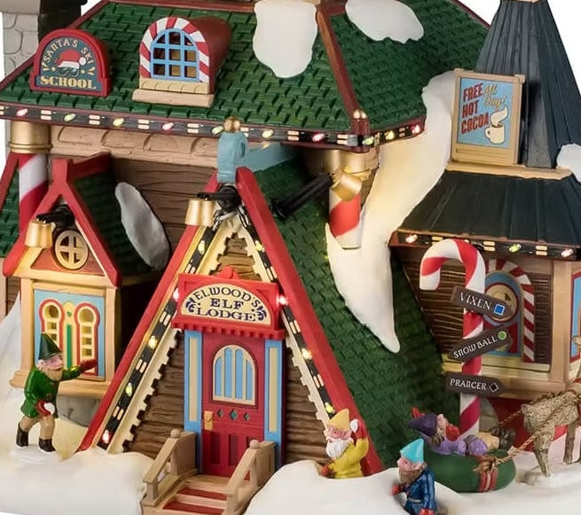 This is an up close view of the building. The sign above the door reads "Elwood's Elf Lodge." There's a sign on the left side that reads "Santa's Ski School." And there's a sign on the right that reads "Free Hot Cocoa!"