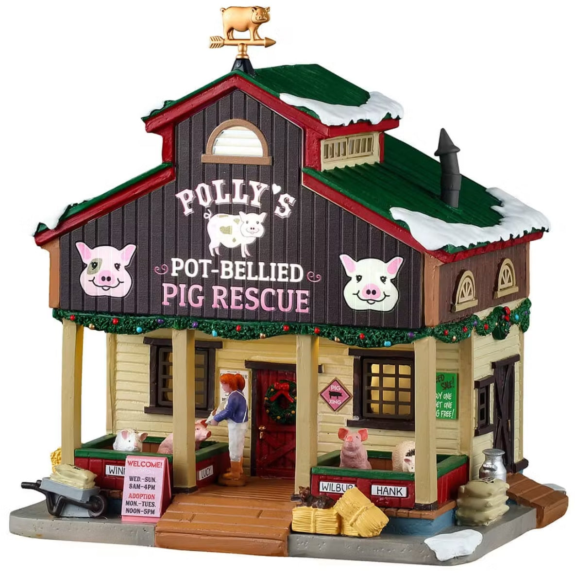 This is a Lemax lighted building designed to look like a barn turned into a pig rescue. There's snow on the roof and on the sidewalk. Polly stands on the front porch feeding the pigs. The pigs are named Winnie, Lucy, Wilbur and Hank. There's hay and bags of feed all over.