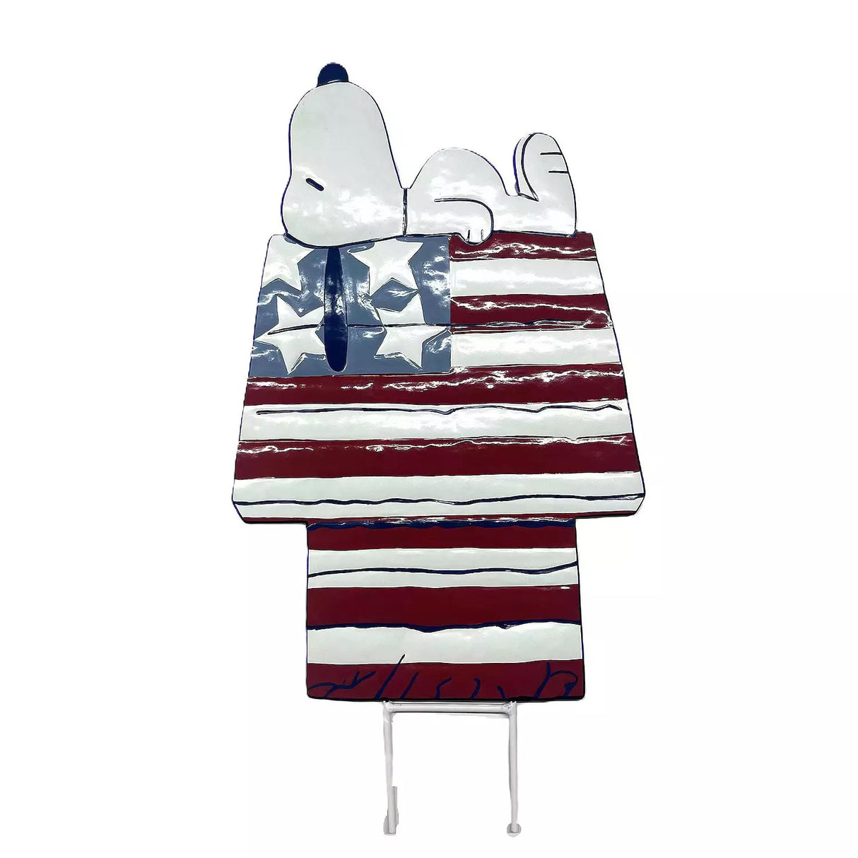 This decorative garden stake is designed to look like the famous Peanuts character, Snoopy. Snoopy is sleeping on top of his doghouse and the house is designed to look like the American flag: red, white and blue stars and stripes.