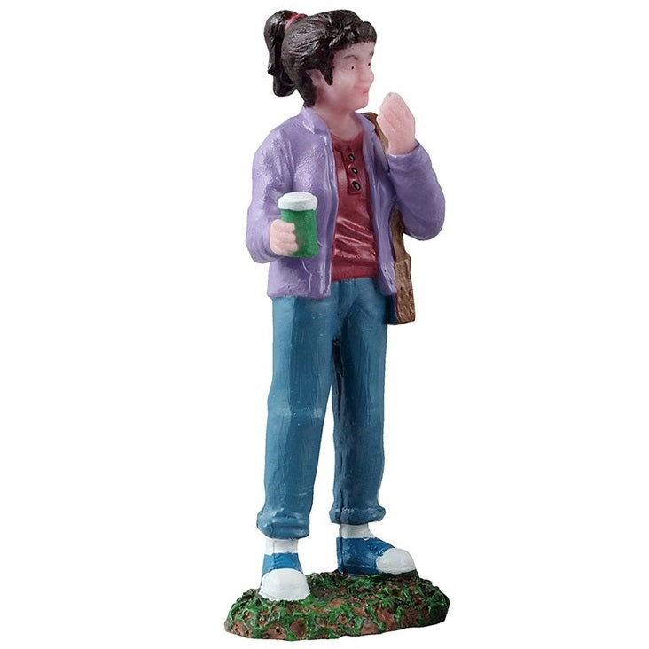 This is the figurine of the girl who is watching. She has brown hair in a pony tail. She's wearing a purple jacket, a red shirt with black buttons, blue jeans and blue and white shoes. She's holding a green cup and a brown purse.