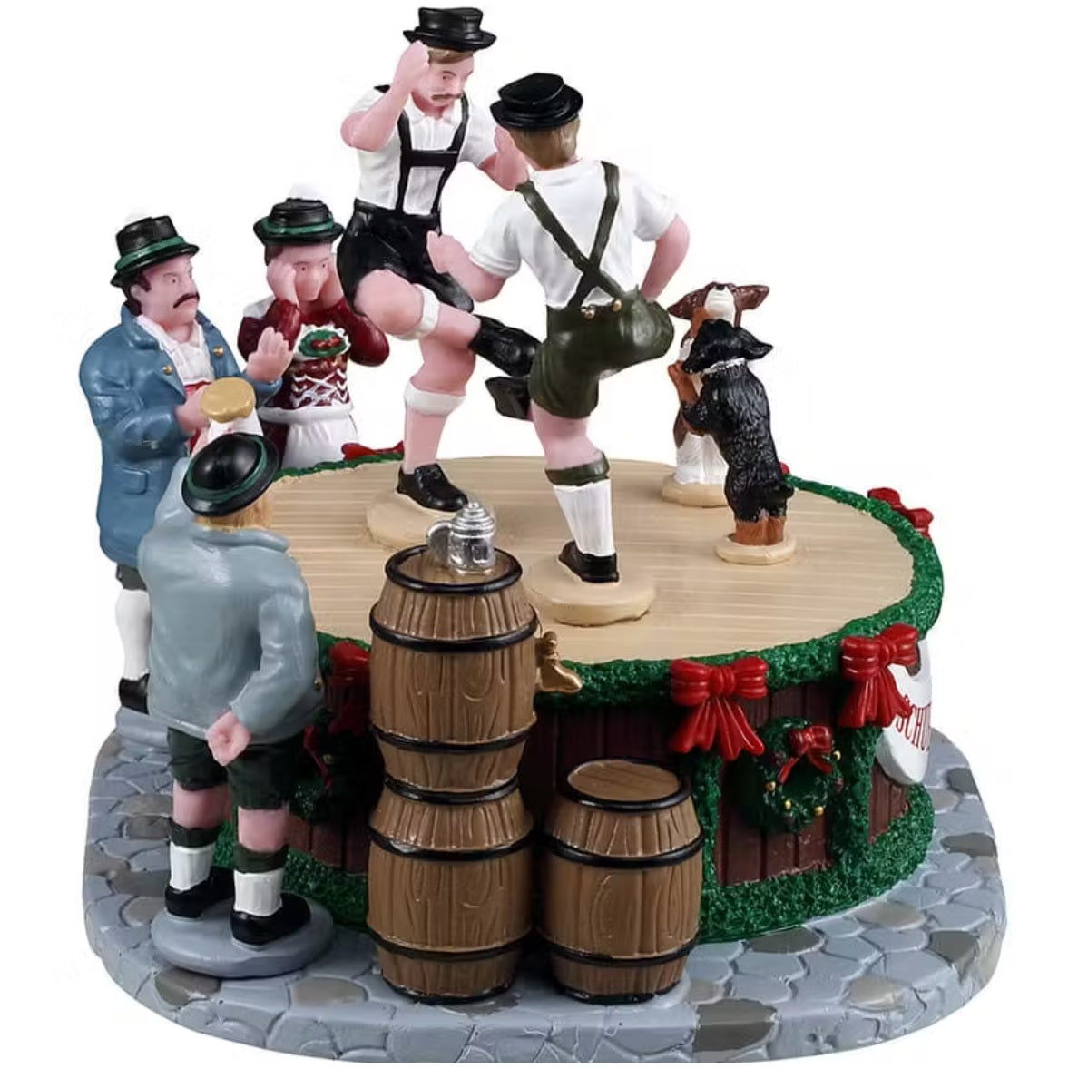 This is a different view of this Lemax piece. The men are on stage in lederhosen and black top hats. The stage is decorated with green garland, red ribbon and wreaths. There are three people standing and watching. There are three wooden barrels on the stone pathway around the stage.