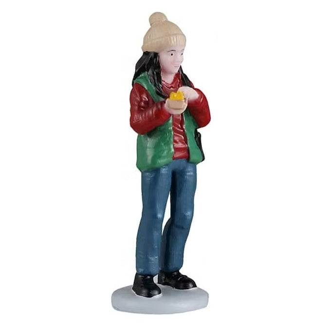 This person is wearing a tan colored winter hat, a red long sleeve shirt, a green vest, blue jeans and black shoes. She's holding food in her hand.