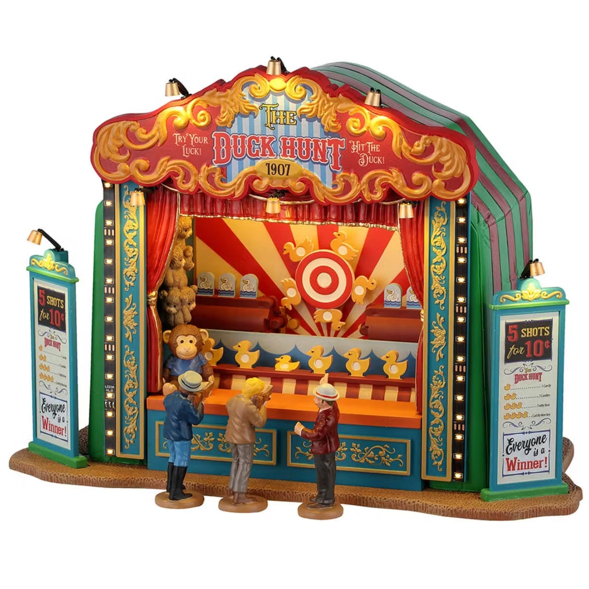 This is a Lemax Carnival piece designed to look like a carnival booth. There are three kids aiming guns at fake ducks that move. The booth is red and green striped with gold accents and lights. Some of the prizes are teddy bears and other toys. There are two signs on each side that read "5 SHOTS FOR 10¢. DUCK HUNT. EVERYONE IS A WINNER!"