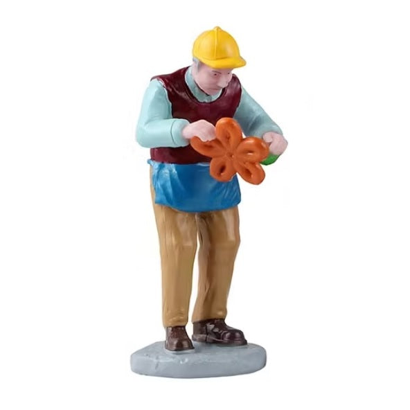 This figurine shows a man bending an orange and green balloon so it looks like a flower.