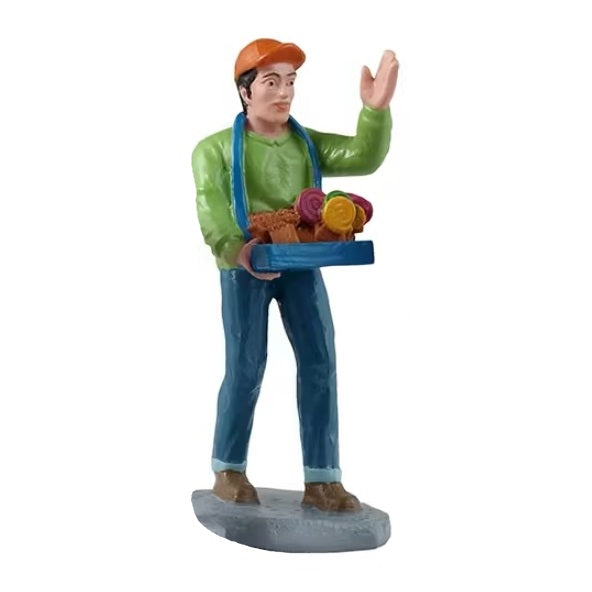This figurine shows a man carrying a tray of treats. He's waving to get people to buy them.