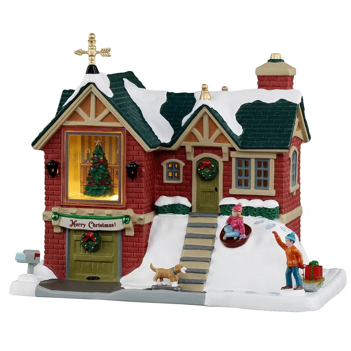 This is a Lemax lighted building designed to look like a two story red brick house. There's a gold weathervane on the roof, along with snow. There's a large window in front and you can see their decorated Christmas tree through it. There are lots of stairs leading up to the front door. There's a wreath on the front door and a banner over the garage door that reads "MERRY CHRISTMAS!" There's a girl in a sled going down the hill and a boy using a sled to pull presents. Their dog is running along on the path.