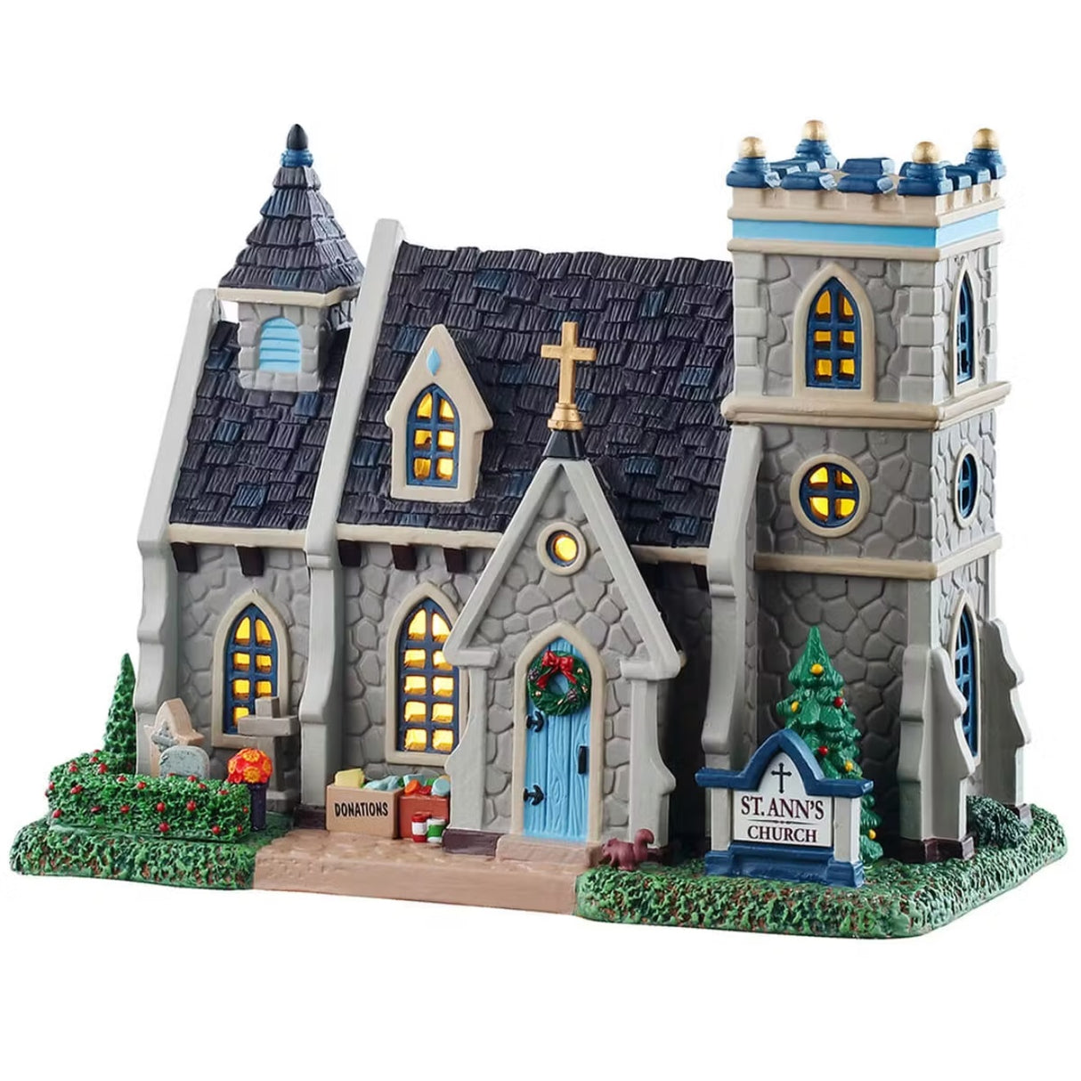 This is a Lemax lighted building designed to look like a stone church. The roof has dark gray shingles. There's a blue front door and blue windows. There's a wreath on the front door and a squirrel digging in the grass in the front. There are flowers and boxes of donations to the right of the door.