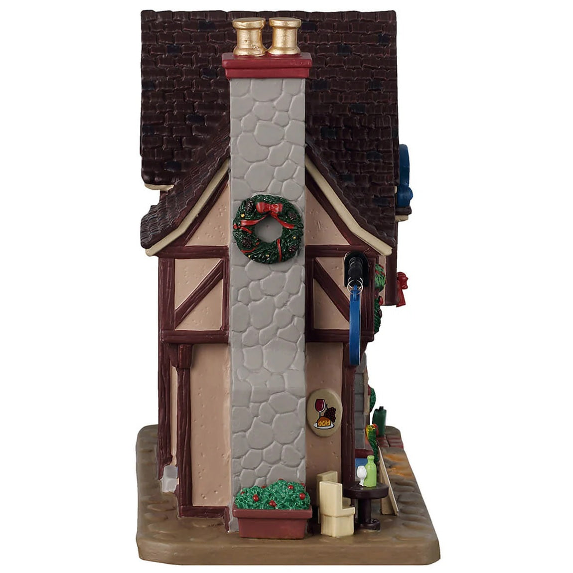 This is the other side of the building. There's a stone chimney with a wreath on it. There's a table and chairs on the sidewalk with a glass of wine on it.