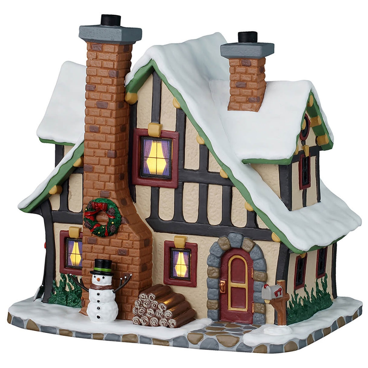 This is a Lemax lighted building designed to look like an old-timey cottage. The sidewalk is made of stone. The snow and the sidewalk is covered in snow. There's a decorated wreath on the red brick chimney and at the base there's a snowman wearing a top hat and a scarf. Next to the door, there's a stack of firewood.