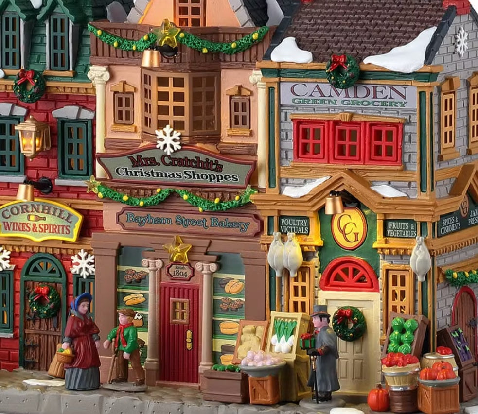 This is a closer view of the building. There are decorated garlands and wreaths decorating the buildings. On the sidewalk, there are three people walking wearing old-timey style clothes.