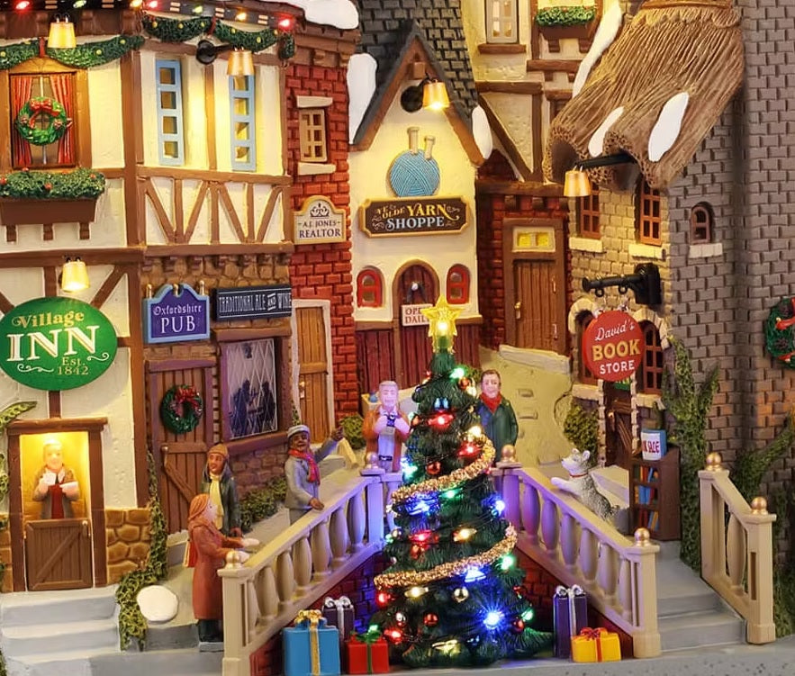 This is an up close view of the building facade. It's decorated for Christmas with wreaths and garland and a large decorated Christmas tree in the center by the stairs. People are gathered around it and there are presents underneath it.