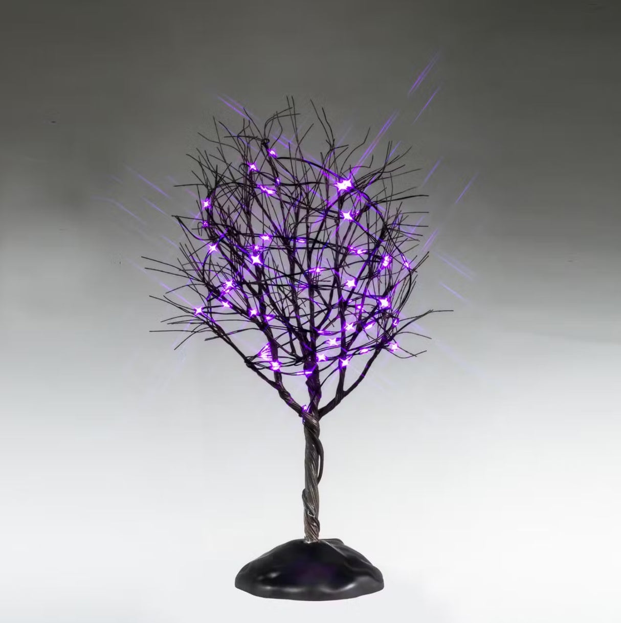This is a Lemax Spooky Town tree that has a twisted trunk, bunches of bare branches and purple lights. This is showing it on a gray background.