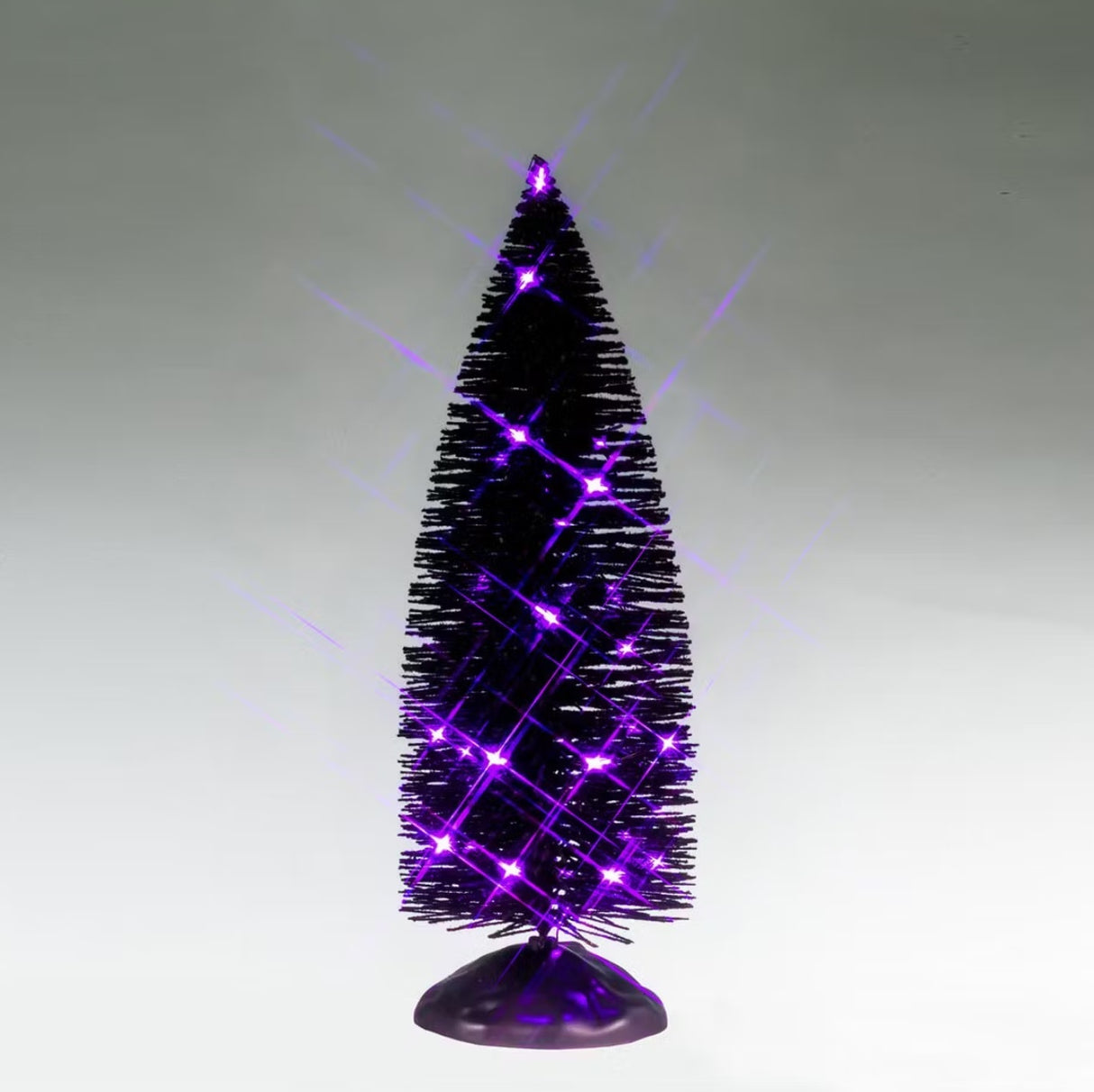 This is a Lemax Spooky Town tree with black bristle branches and it's lit up with purple lights. This is showing it on a gray background.