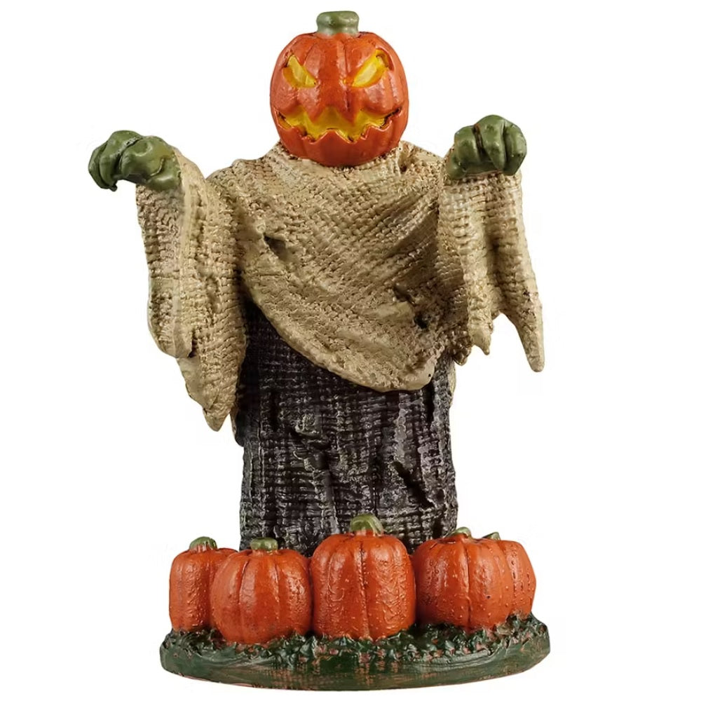 This is a Lemax Spooky Town figurine designed to look like a monster with a jack-o-lantern head and green hands. He's wearing a tan colored shroud with a dark brown shroud underneath. There are pumpkins at the base.