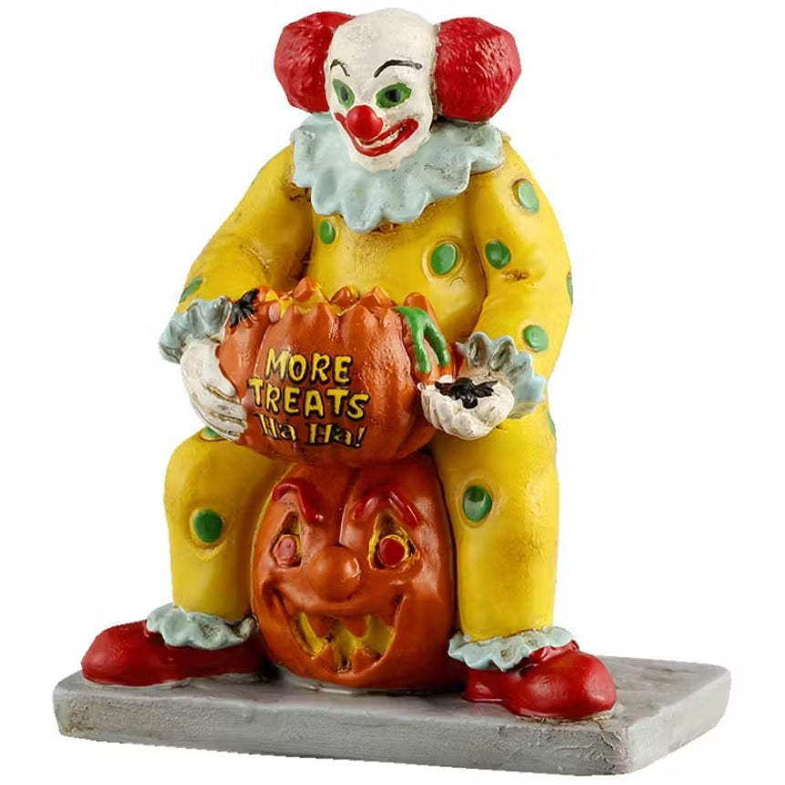 This is a Lemax Spooky Town figurine designed to look like a smiling clown sitting on a carved jack-o-lantern. He's got two red afros on his head and is wearing a yellow jumpsuit with lime green polka dots. He's holding a pumpkin with bugs and slime inside. On the pumpkin it reads "MORE TREATS HA HA!"