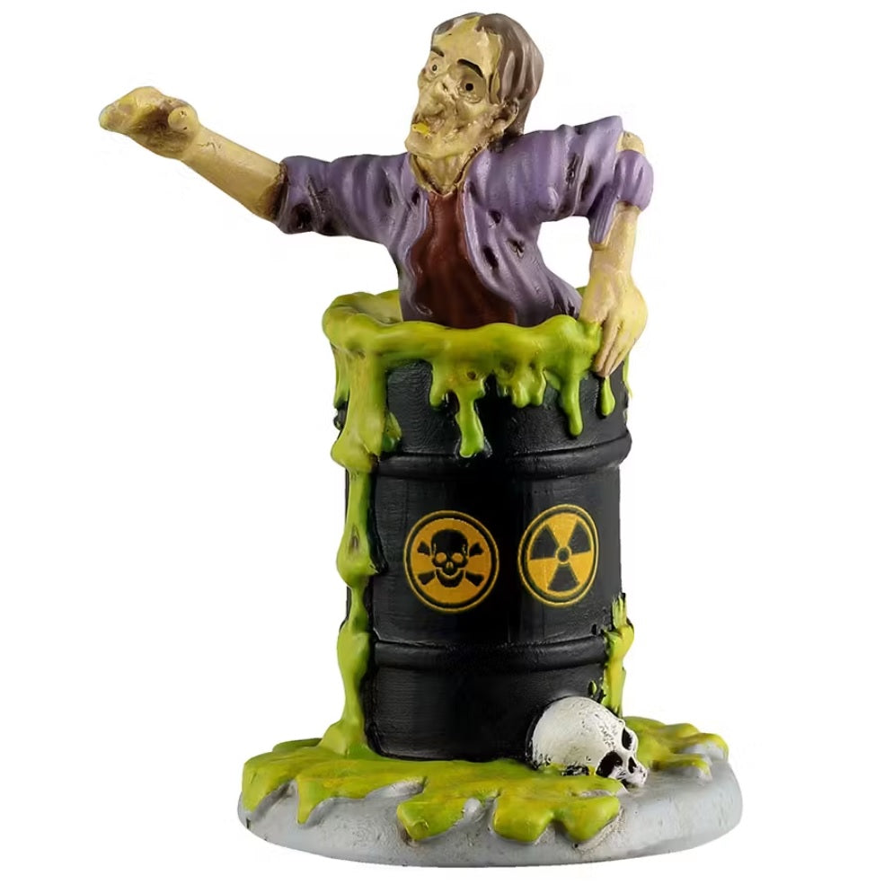 This is a Lemax Spooky Town figurine that's designed to look like a zombie man coming out of a black barrel that has green sludge coming out of it. There's a white skull at the base. There are two bio-hazard warnings on the barrel.