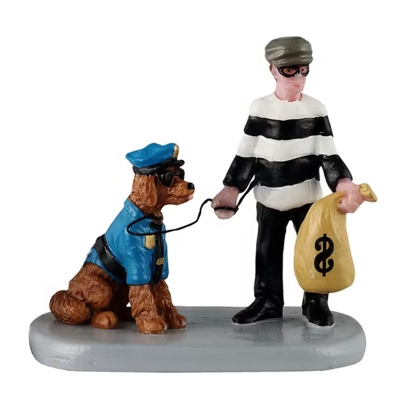 This figurine shows a young boy dressed as a robber, wearing a black eye mask, a white and black striped sweater and he's holding a brown bag with a dollar sign on it. He's holding a leash attached to a dog who is dressed up as a cop. The dog is wearing a blue police uniform and sunglasses.