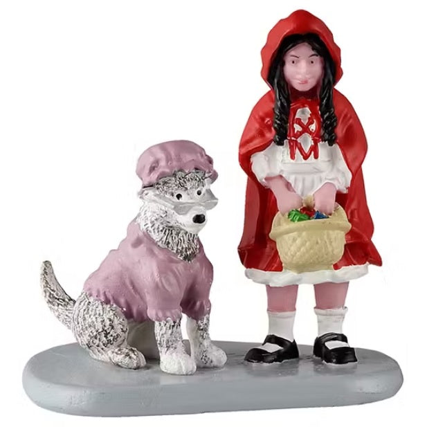 This figurine shows a young girl dressed as Little Red Riding Hood carrying a basket of food. Next to her is a dog dressed up like Little Red Riding Hood's grandma in a pink nightgown and bonnet and a pair of glasses resting on her nose.