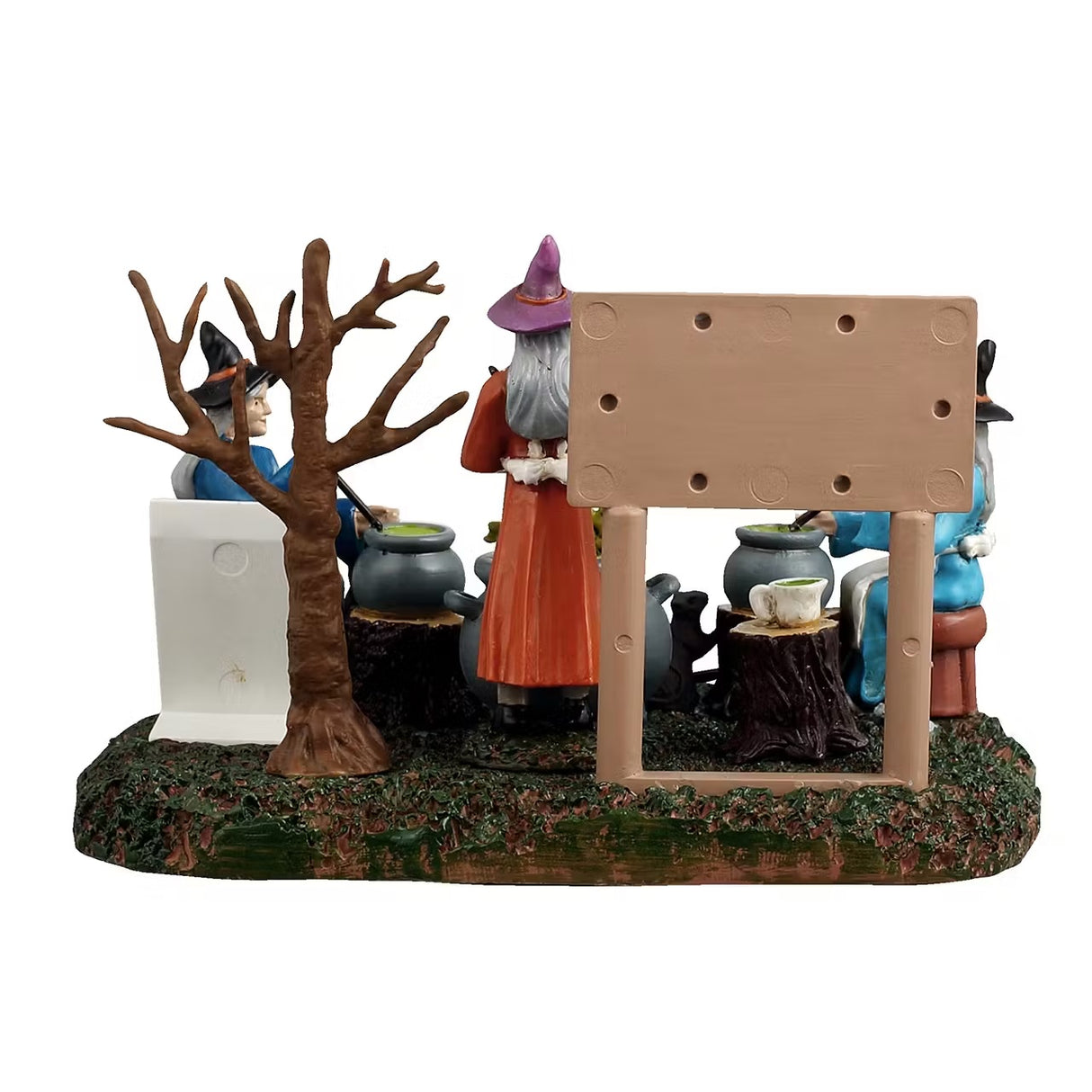 This is a different angle of the Lemax Spooky Town table accent designed to look like three witches sitting around stirring their individual cauldrons. There's a white board that reads "TOAD SOUP. Ingredients: 3 toads, 1 cup of swamp water, 1 cup of flies and 1 cup of worms." One witch is sitting on a stool and is wearing a blue cloak with a black hat. One witch is sitting on a tree stump and is wearing a dark blue cloak with a black hat. One witch is standing and is wearing an orange cloak with a pink hat.